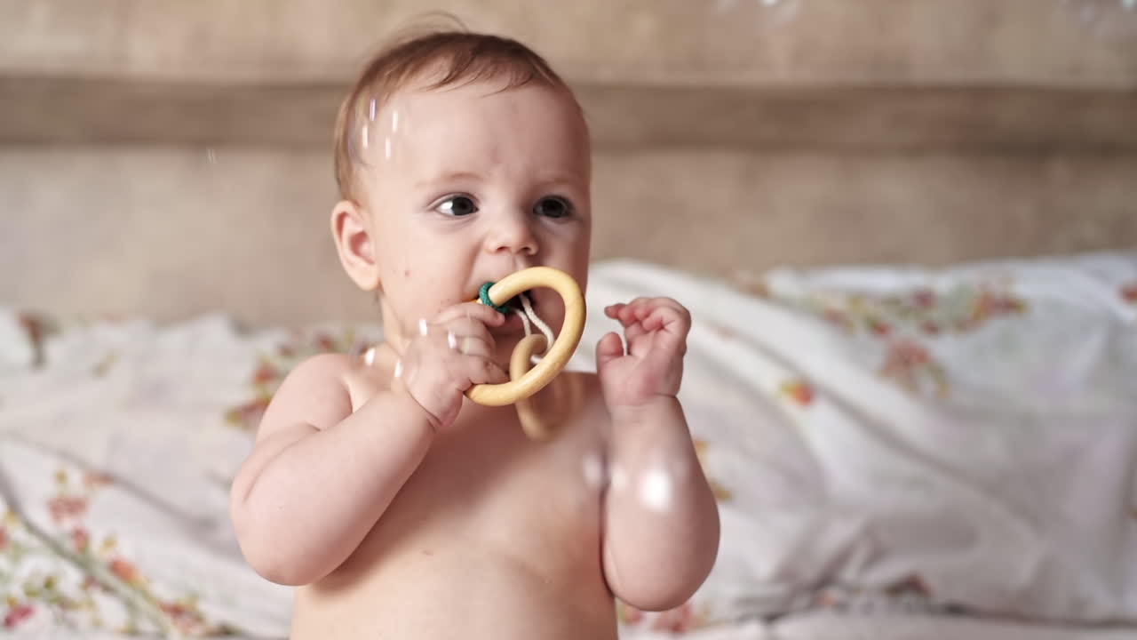 Caucasian blonde baby boy on a bed, playing with toys. Soap bubbles flying around