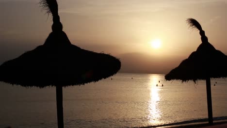 escena de la playa al atardecer con sombrillas de paja
