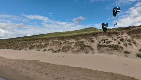 cinematic tracking shot showing couple of paraglider soaring over beach and coastline of netherlands - spectacular drone sport footage