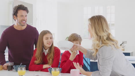 parents helping children in school uniform get ready as they eat breakfast at kitchen counter