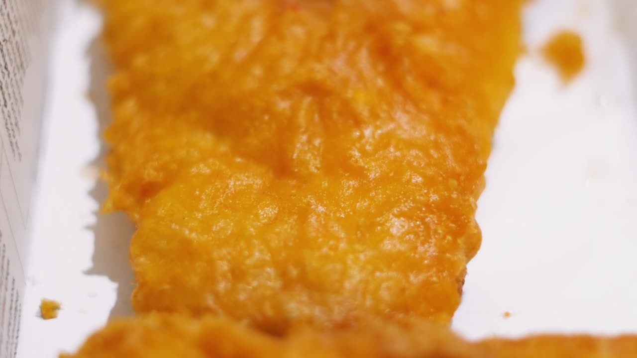 Crispy Details of British Battered Cod in Takeaway Box as Camera Slowly Moves Down Fillet of Fish. Deep Fried Fresh Cod Seafood Served in Britain