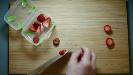 strawberries being sliced on a bamboo chopping board