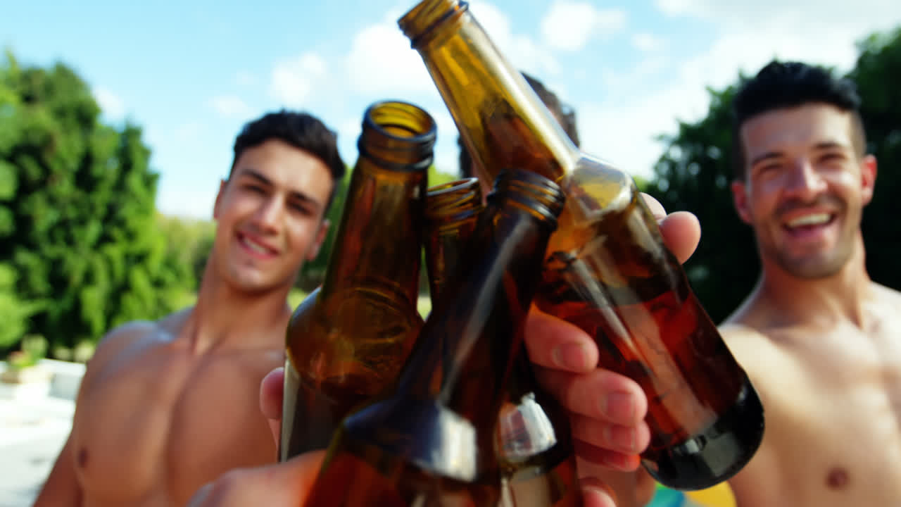 grupo de amigos masculinos brindando botellas de cerveza junto a la piscina