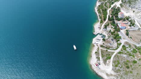 Costa-De-La-Prístina-Playa-De-Pula-De-La-Bahía-Azul-Del-Mar-En-Rakalj-Croacia,-Vista-Aérea-De-Drones-Sobre-Un-Barco-Solitario-En-Un-Increíble-Paisaje-Marino-Pacífico