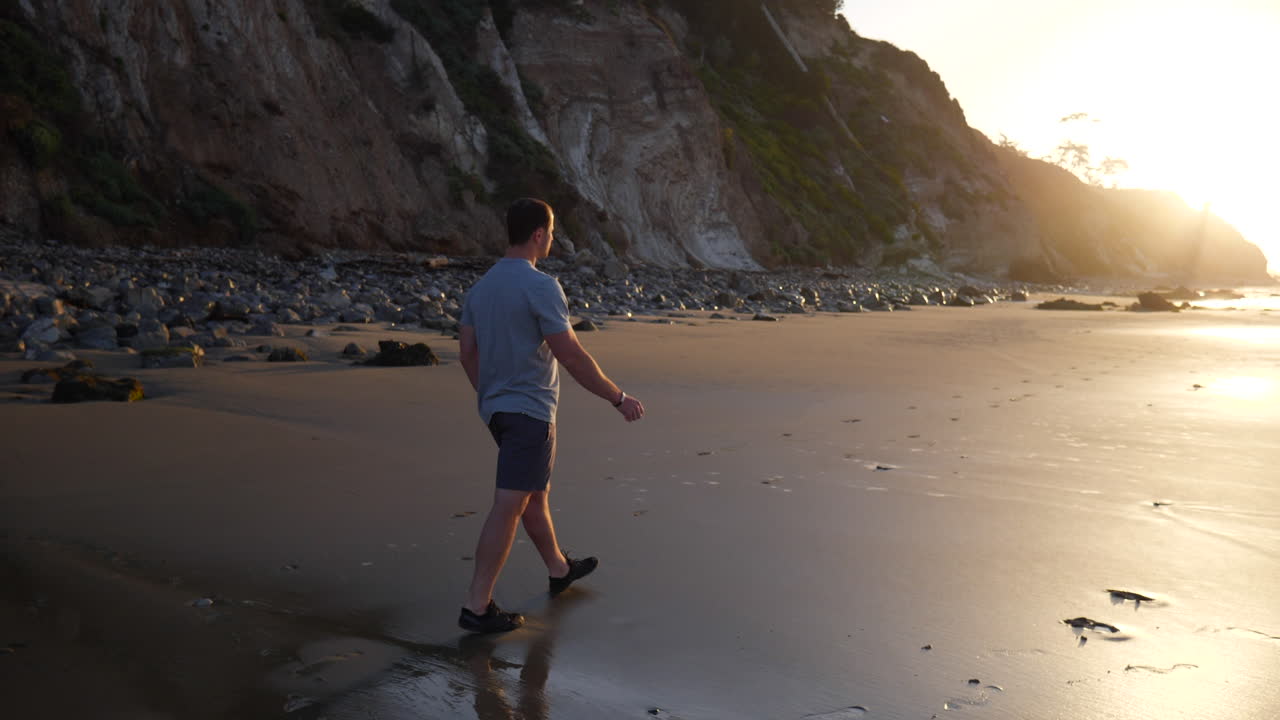 un joven fuerte caminando por la playa después de un entrenamiento físico matutino al amanecer en santa barbara, california a cámara lenta