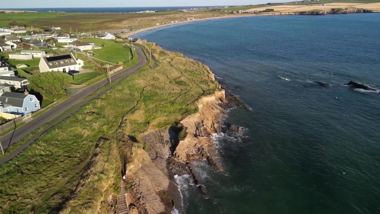 Garrylucas strand, klipper og vej med huse og sommerhuse set ovenfra. Luftfoto af County Cork i Irland på en solrig, rolig dag.