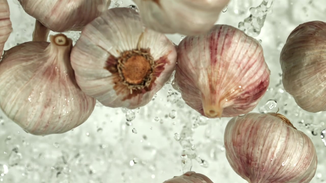 Teste d'aglio fresche che schizzano nell'acqua al rallentatore