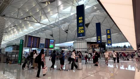 travelers move through a busy airport terminal in hong kong, with visible gate information and departure boards.
