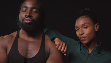 close up studio portrait of smiling athletic couple or friends in fitness clothing training shot against black background