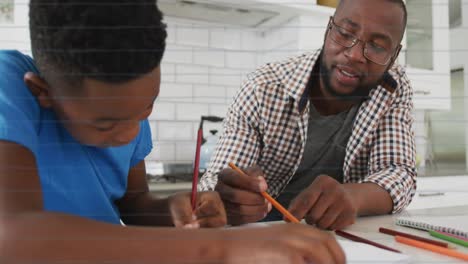 Animation-of-school-icons-over-father-and-son-doing-homework-together