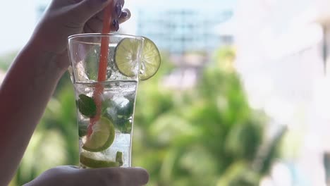 woman-stirs-cold-mojito-cocktail-with-orange-straw