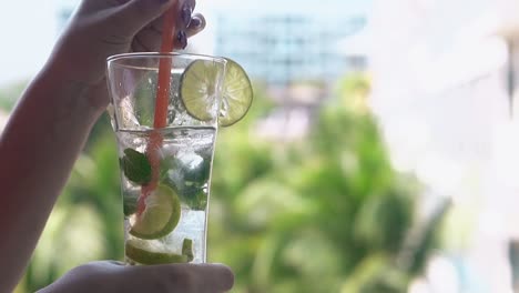 mujer agita cóctel de mojito frío con paja de naranja