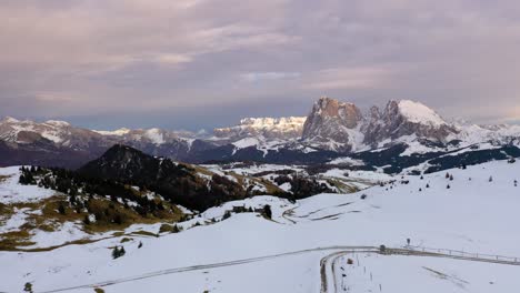 Toma-Aérea-De-La-Carretera-En-La-Nieve-Que-Conduce-A-Una-Vista-Panorámica-De-La-Cordillera-En-El-Prado-Alpino-Seiser-Alm---Alpe-Di-Siusi-En-Los-Dolomitas,-Italia