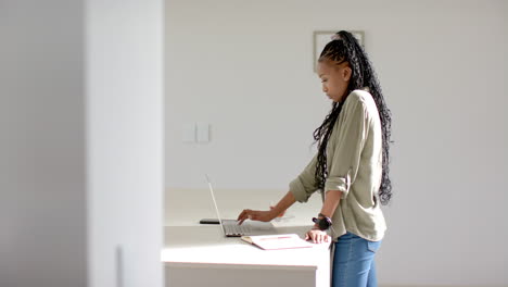 African-American-young-woman-standing,-using-laptop-on-white-desk