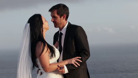 recent newlyweds married couple showing affection hugging carressing kissing and loving each other on wedding day sunset beach sea coast bridal photoshoot location close up slow motion color graded hd