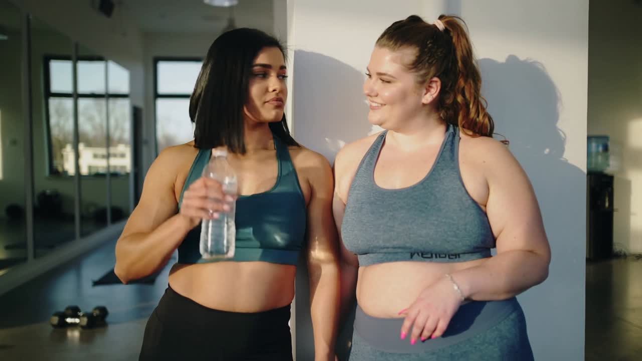 La donna a sinistra che beve dalla bottiglia, la donna a destra che si asciuga il viso dopo l'allenamento in studio e in abbigliamento sportivo.