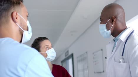 diverse doctors wearing face masks, discussing work in corridor at hospital, slow motion