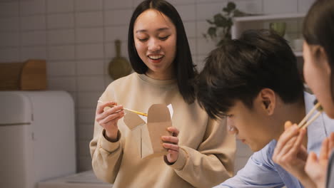 happy japanese woman holding chopsticks while eating ramen in the kitchen