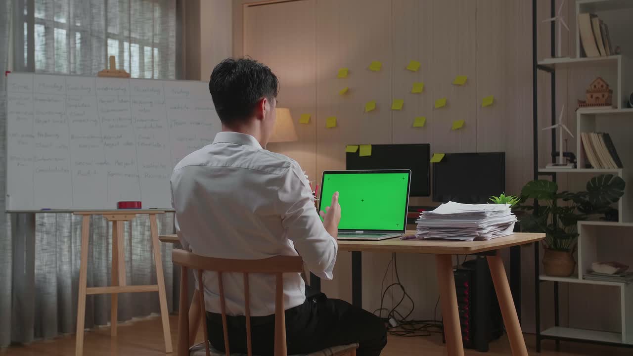 사무실 에서 문서 를 처리 하는 동안 녹색 스크린 노트북 과 대화 하는 아시아인 의 뒷면