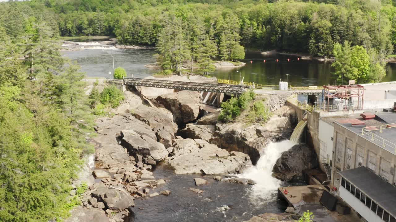 Aerial view over a river water flowing through an hydro electric dam, surrounded by forest