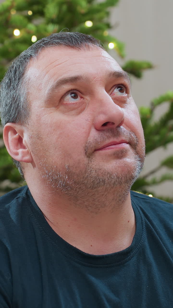 Caucasian man with snowdusted beard, cozy living room framed by twinkling tree lights candid closeups move from contemplative glance to gentle smile as man acts as home decorator, quiet storyteller