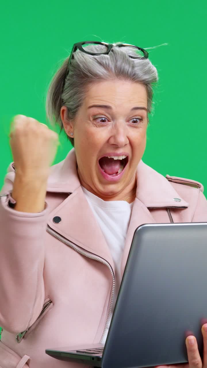 Donna matura reagisce con sorpresa e gioia al contenuto del laptop su schermo verde.