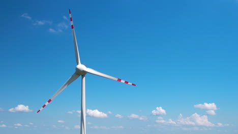 A-spinning-wind-turbine-against-a-sky-blue-sky-with-small-clouds