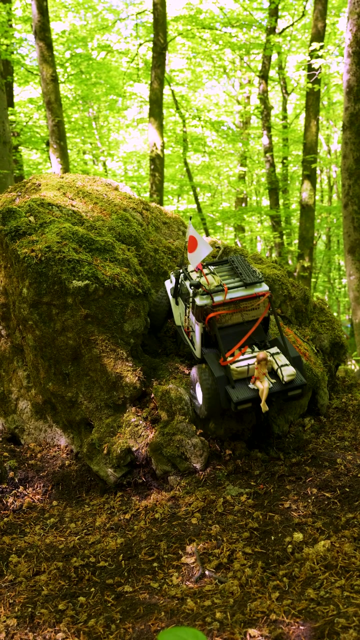 Veicolo fuoristrada telecomandato che scala un ostacolo di roccia muschiosa su un sentiero di gara nel bosco, verticale