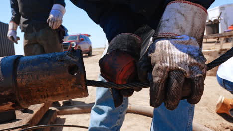 unrecognized man in big protective gloves attaches the detail on the thick metal wire. worker sets the equipment at drilling site. close up.