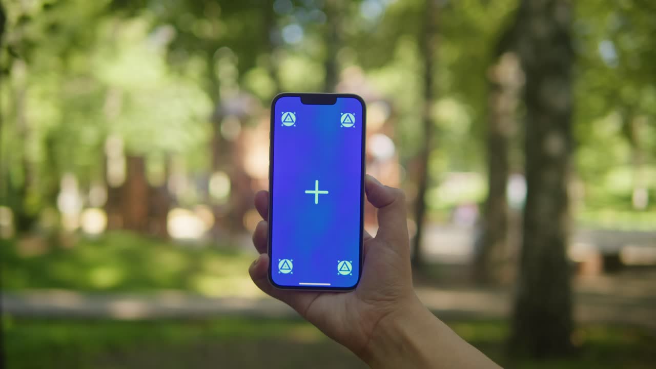 Young woman holding phone chroma key screen in the park close-up. Girl with green screen on smart phone. Nature