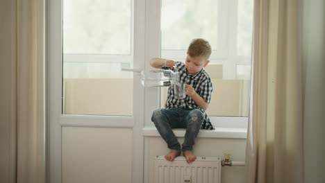 boy pouring water from a jug into a glass on a window sill.