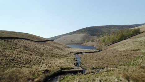 aerial shot close to the ground of a stream following it downstream to the mouth of kinder reservoir, peak district, uk