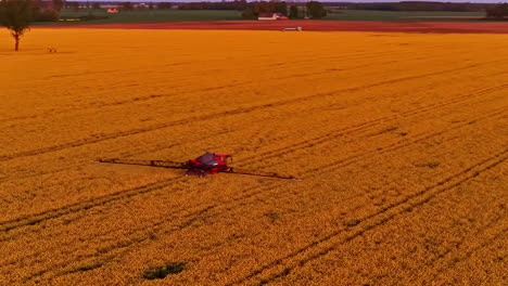 Farming machine sprays golden field at sunset, aerial view of rural agriculture work