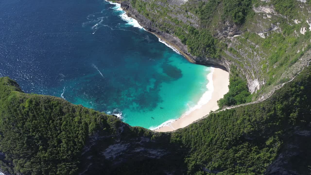 Drone footage capturing a wide aerial orbit of Kelingking Beach in Bali, Indonesia, highlighting the turquoise waters, dramatic cliffs, and the surrounding landscape