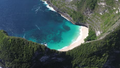 drone footage capturing a wide aerial orbit of kelingking beach in bali, indonesia, highlighting the turquoise waters, dramatic cliffs, and the surrounding landscape