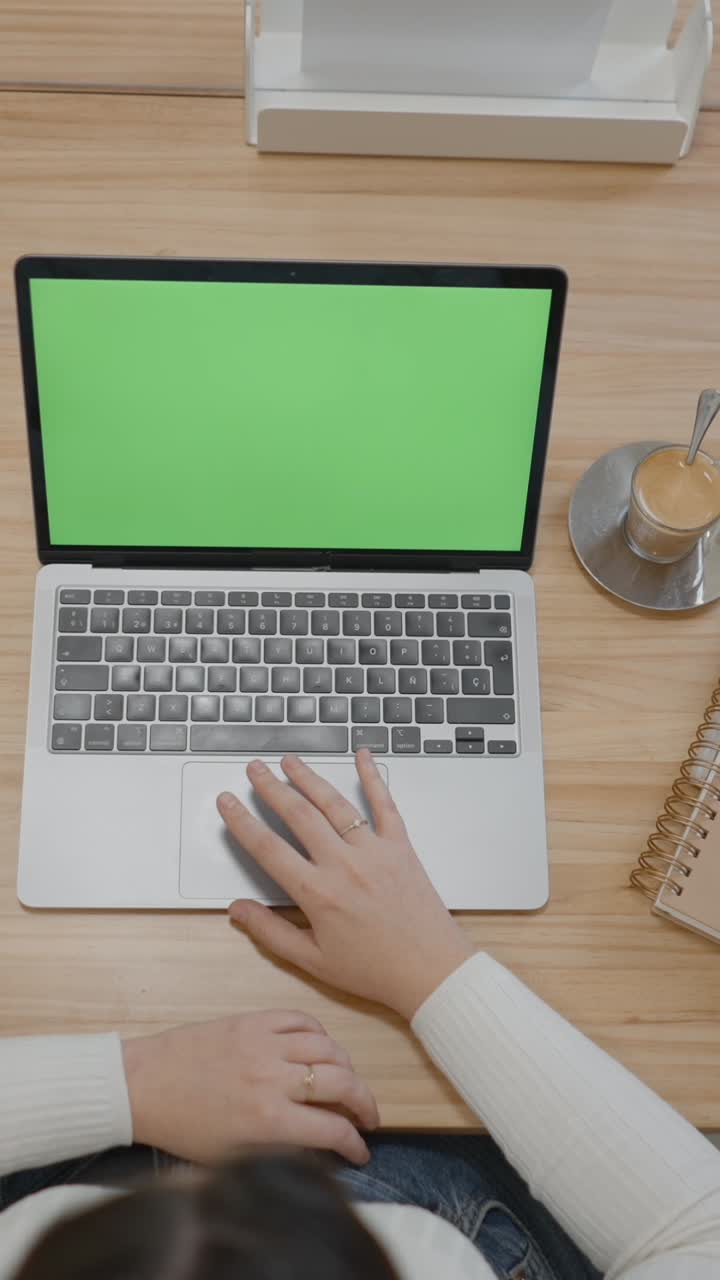 Person working on a laptop with a green screen on a wooden desk