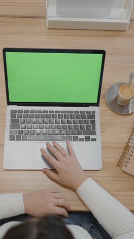 person working on a laptop with a green screen on a wooden desk