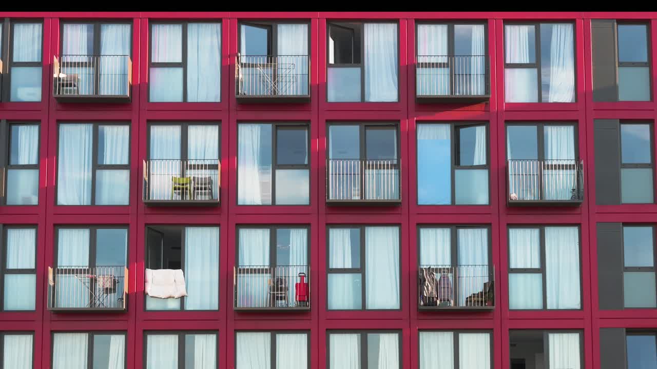 Modern red facade of a residential building in Barcelona, Spain. Geometric pattern of windows and balconies highlighting contemporary urban architecture