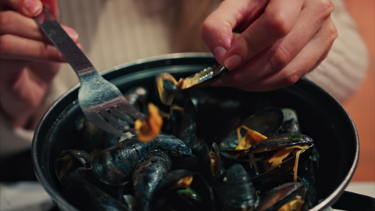 Close up of a woman eating mussels from a pan with a fork