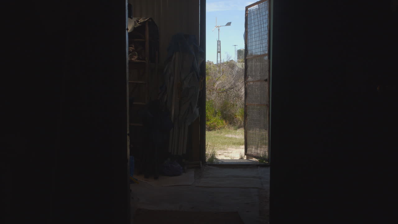 View from a Shed's Open Door to a Coastal Landscape with Wind Turbine