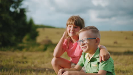 brother and sister squatting outdoors in warm sunlight, sharing a close sibling moment, sister affectionately holds her brother as they enjoy peaceful countryside setting