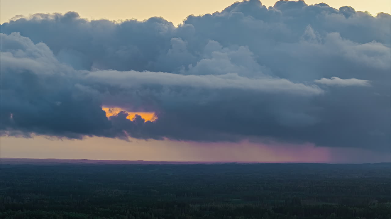 Dark storm clouds rolling over distant landscape with streaks of rain and a warm glow breaking through the cloud layer in a dramatic timelapse sky
