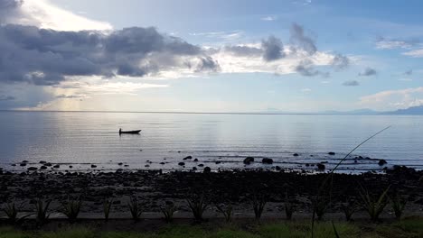 A-solo-fishermen-on-a-traditional-wooden-fishing-canoe-paddling-through-ocean-in-early-morning-light-on-Atauro-Island,-Timor-Leste