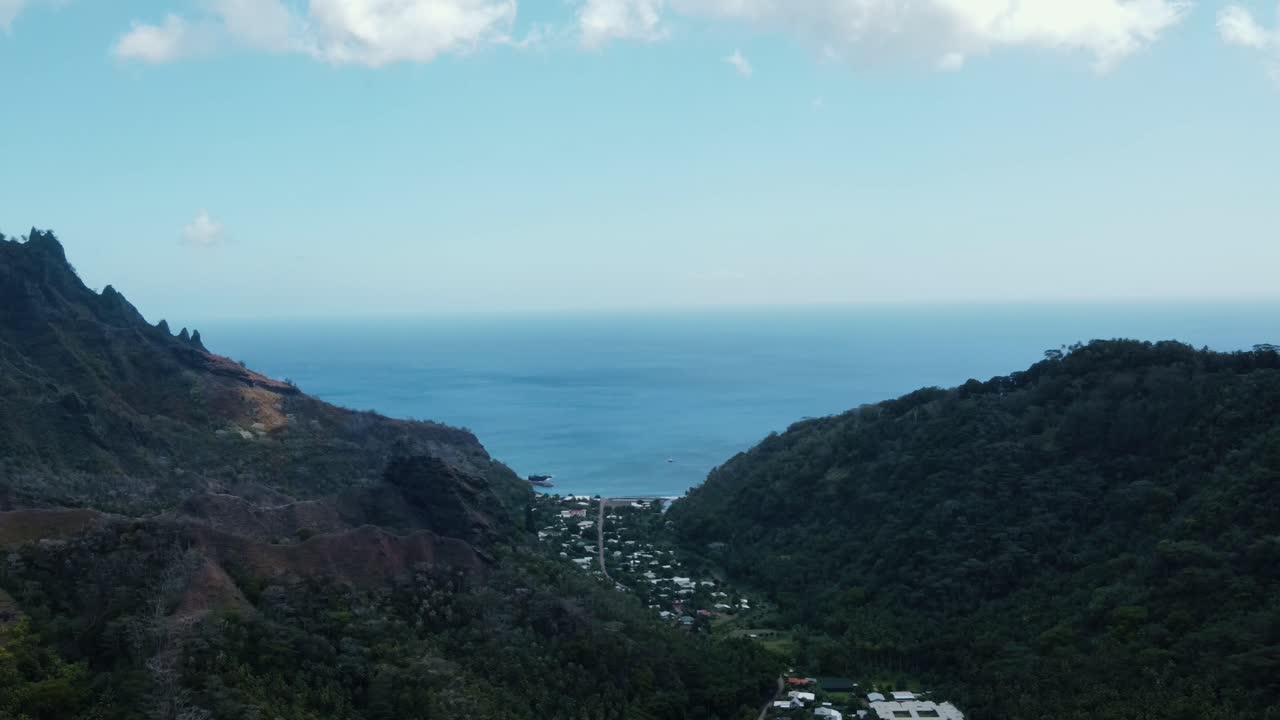 마르케사스 남태평양 프랑스 폴리네시아의 파투 히바 섬의 버진 만의 푸른 산 사이에 자리 잡은 폴리네시아 마을과 함께 육지에서 볼 수 있습니다.