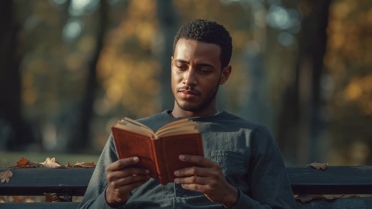 Mann mit langärmligem Hemd und dünner Kette, der ein gebundenes Buch liest, hebt den Kopf und lächelt auf einer Parkbank