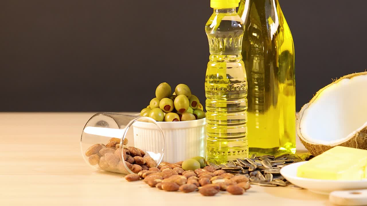A variety of healthy fats and oils, including avocados, coconut, and olive oil, arranged on a wooden table with soft lighting