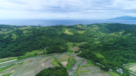 wide panning aerial shot of a farm beside the mountains, nearby sea