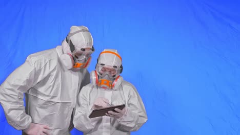 científico virólogo en respirador hace escribir en una tableta con lápiz. hombre y mujer con máscara médica protectora. clave de croma azul.