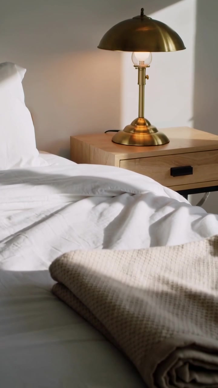 Vertical video: Panning camera revealing brass lamp and bed folds to show subtle light, copy space