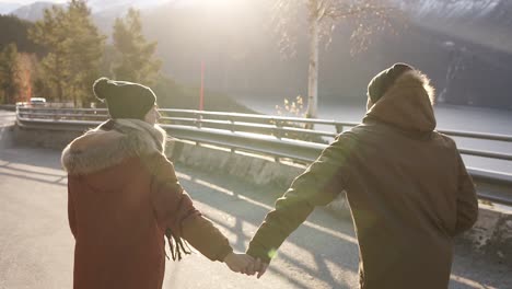 the couple looking forward to the adventure. together they run along an asphalt road or a highway in winter among the norwegian mountains. rare view. sun shining and lake on the background